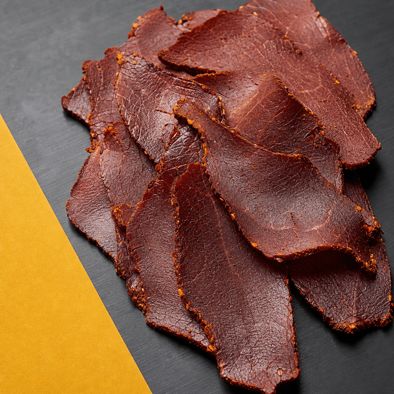 Thin irregular slices of seasoned air-dried beef on charcoal metal beside yellow paper