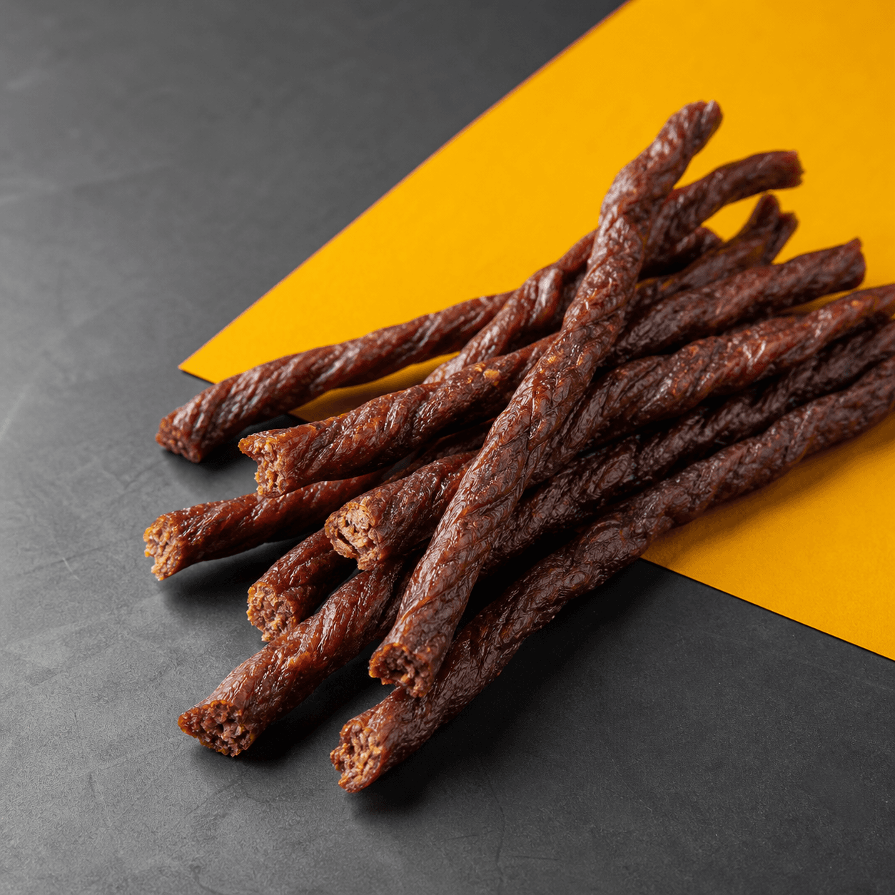 A loose bundle of thin twisted dried-meat sticks on charcoal metal and yellow paper